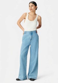 Jasnoniebieskie dżinsy o szerokich nogawkach i wysokim stanie, z klasycznym pięciokieszeniowym fasonem, zestawione z białym topem na ramiączkach. Gładka faktura denimu.