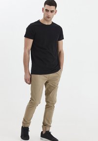 Camiseta negra de manga corta, ajuste slim, combinada con pantalones beige ajustados con puños elásticos, usados con zapatillas negras.