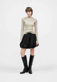 Béžový žebrovaný svetr s unikátním detailem na ramenou, zkombinovaný s černou balónovou sukní a černými kozačkami pod kolena. Jednoduchý a moderní design.