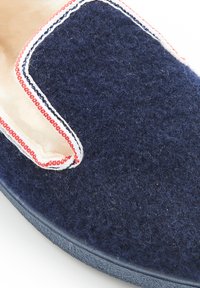 Marineblauwe vilten slipper met een luxe textuur, voorzien van een crèmekleurig interieur en contrasterende rode en witte stiksels langs de randen.