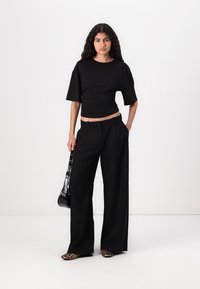 Sort cropped top med korte ærmer, parret med højaldede sorte bukser med bred ben. En sort taske og sko med dyreprint fuldender looket.