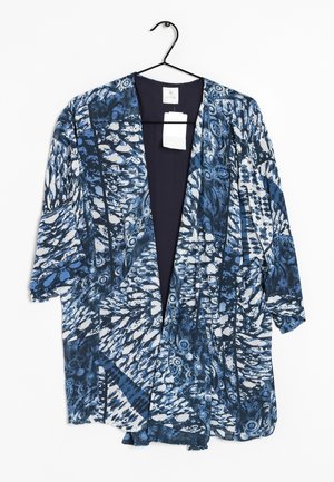 Niebiesko-biały kardigan w stylu kimono z abstrakcyjnym wzorem i rękawami do połowy przedramienia, wiszący na czarnym wieszaku na białym tle.
