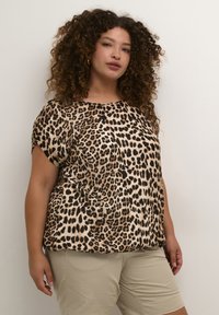 Haut ample à imprimé léopard beige, avec des manches courtes et un col rond. Texture douce, associé à un short beige clair.