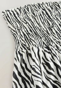 Tkanina s uzorkom zebra u crno-bijeloj boji s nabrano-ručnim vrhom i prozračnom teksturom. Ima vertikalne pruge i nabrani struk.
