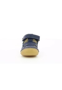 Zapato infantil de color azul marino con correa de velcro, paneles laterales de malla texturizada y suela de goma. Presenta costuras blancas y diseño de punta redondeada.