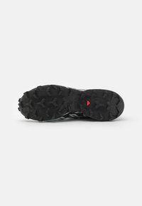 Talpa de pantof sport în nuanțe de negru și gri, cu un model texturat și striaturi adânci. Accent roșu aproape de călcâi. Material din cauciuc conceput pentru aderență.