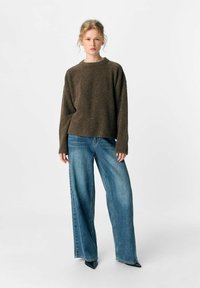 Brauner, übergroßer Strickpullover mit fällt Schultern, kombiniert mit weiten blauen Denim-Jeans und spitzen schwarzen Schuhen. Einfaches, strukturiertes Design.