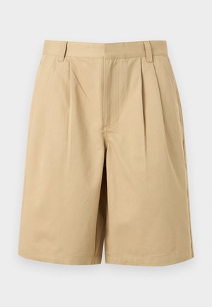 Smėlio spalvos kelių ilgio šortai su priekinėmis klostėmis, diržo kilpelėmis ir paslėptu priekinio užsegimo mechanizmu, rodomi ant vienspalvio fono.