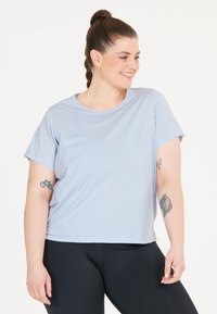 Ljusblå kortärmad t-shirt, tillverkad av mjukt tyg, med rund halsringning. Bärs med svarta leggings, som visar tatueringar på armen.