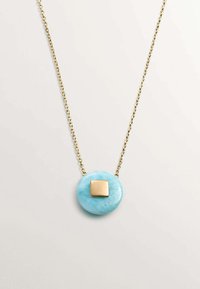 Collar de cadena de oro con un colgante redondo de color azul claro con una superficie texturizada y un acento cuadrado de oro en el centro.