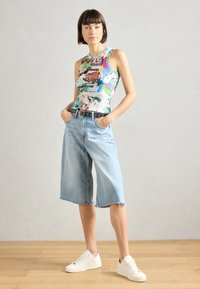 Χρωματιστό γραφικό αμάνικο μπλουζάκι με ριγωτή υφή, συνδυασμένο με ανοιχτό μπλε τζιν culottes με ξεφτισμένα τελειώματα και μια μαύρη ζώνη με κυκλικά στοιχεία. Λευκά αθλητικά παπούτσια.