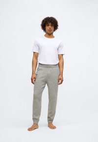 Γκρι παντελόνι φόρμας από ανάμεικτο μάλλινο ύφασμα με ελαστική μέση και ριμπ μανσέτες, συνδυασμένο με ένα απλό λευκό κοντομάνικο μπλουζάκι. Γυμνά πόδια.