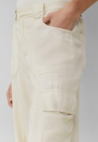 Beige cargo broek van textuurstof, met zijzakken en een relaxte pasvorm. Stikdetails zichtbaar langs de naden.