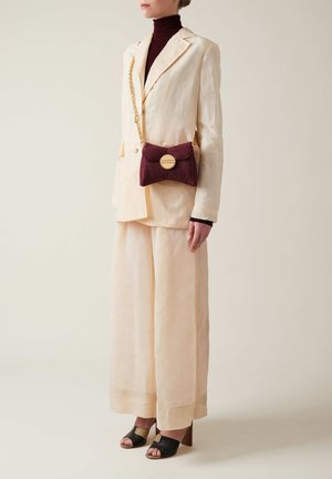 Beige linen suit with wide pants, paired with a dark turtleneck. A burgundy textured handbag with a gold chain and circular clasp accent.