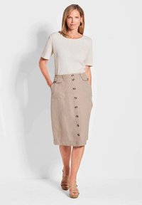 Beige Leinenrock mit Frontknöpfen, zwei Seitentaschen und einem taillierten Bund. Kombiniert mit einem kurzärmeligen weißen Oberteil und beigen Sandalen mit Riemchen.