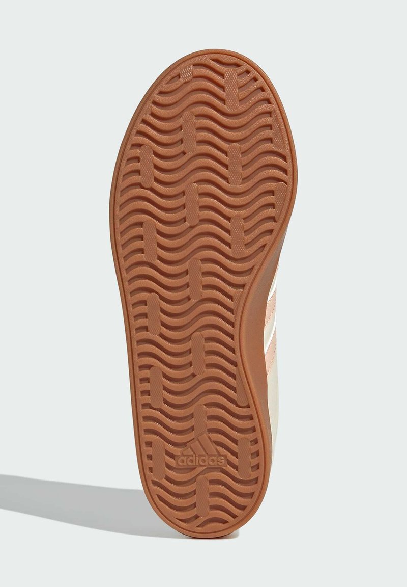 Semelle de sneaker Adidas, présentant un motif ondulé et texturé en caoutchouc marron. Les côtés comportent des rayures blanches sur un fond crème.