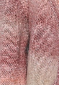 Kötött pulóver, amely lágy rózsaszín és krémszínű színátmenetet mutat, texturált, kényelmes megjelenéssel és laza fazonnal.