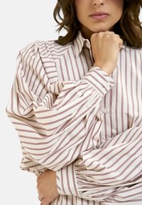 White shirt with maroon stripes, buttoned up with a structured collar and voluminous, gathered sleeves, displaying a soft, smooth texture.