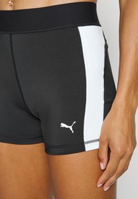 Gros plan sur une personne portant un short de sport Puma noir et blanc, montrant la taille, la bande latérale et le logo Puma.