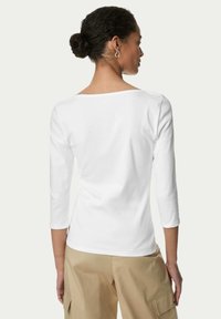 Hvid bomulds langærmet skjorte med rund halsudskæring, tætsiddende silhuet og let samling ved skulderen, kombineret med tan-farvede bukser med vide ben.