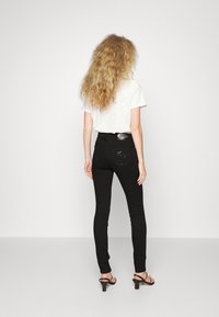 Svarta högmidjade skinny jeans med en glansig textur, med en design på bakfickan och kombinerade med en enkel vit T-shirt och svarta klackar.