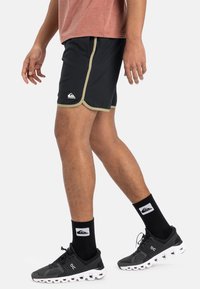 Svarte treningsshorts med kontrasterende lysgrønn kant, med logo på det nederste av benet. Båret med svarte sokker og sporty sko.