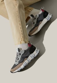 Baskets avec un mélange de gris, noir et beige ; tige texturée, col rembourré et lettres en gras "VOILE BLANCHE" sur la semelle.