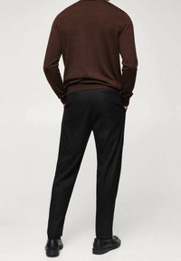 Maglione marrone a maglia con scollatura rotonda, abbinato a pantaloni neri con una texture liscia e tasche. Le scarpe nere completano l'outfit.