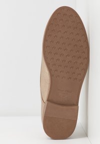 Semelle d'une chaussure beige avec un dessous en caoutchouc texturé présentant un motif répétitif "AF", nom de la marque ANNA FIELD, et taille 37 au niveau du talon.