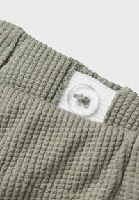 Grijze textuurstof met een geribbelpatroon, voorzien van een witte sectie en een heldere knoopdetail op de taille.