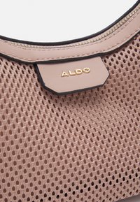 Rosa nätväska med en strukturerad, perforerad design. Har en svart läderdetalj och en gyllene "ALDO"-logotyp på en beige lapp.