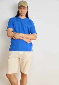 T-shirt en coton bleu et shorts cargo beige avec poches latérales. Le t-shirt a un col rond ; les shorts ont une texture lisse.