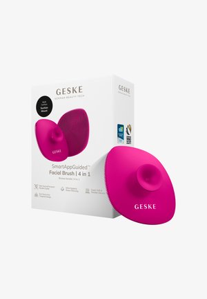 Felroze siliconen gezichtsborstel met zuignap, naast witte verpakking met het label "GESKE SmartAppGuided Facial Brush 4 in 1" en prijsstickers.