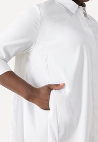 Camicia bianca a maniche lunghe con colletto e tasche laterali. Tessuto morbido, taglio dritto, con un design classico.