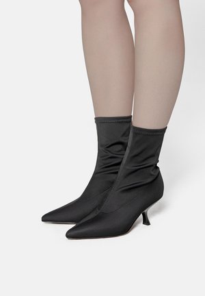 Stivali alla caviglia in satin nero con design arricciato, punta affusolata e tacco kitten di piccole dimensioni. Presenta cuciture visibili lungo le cuciture.