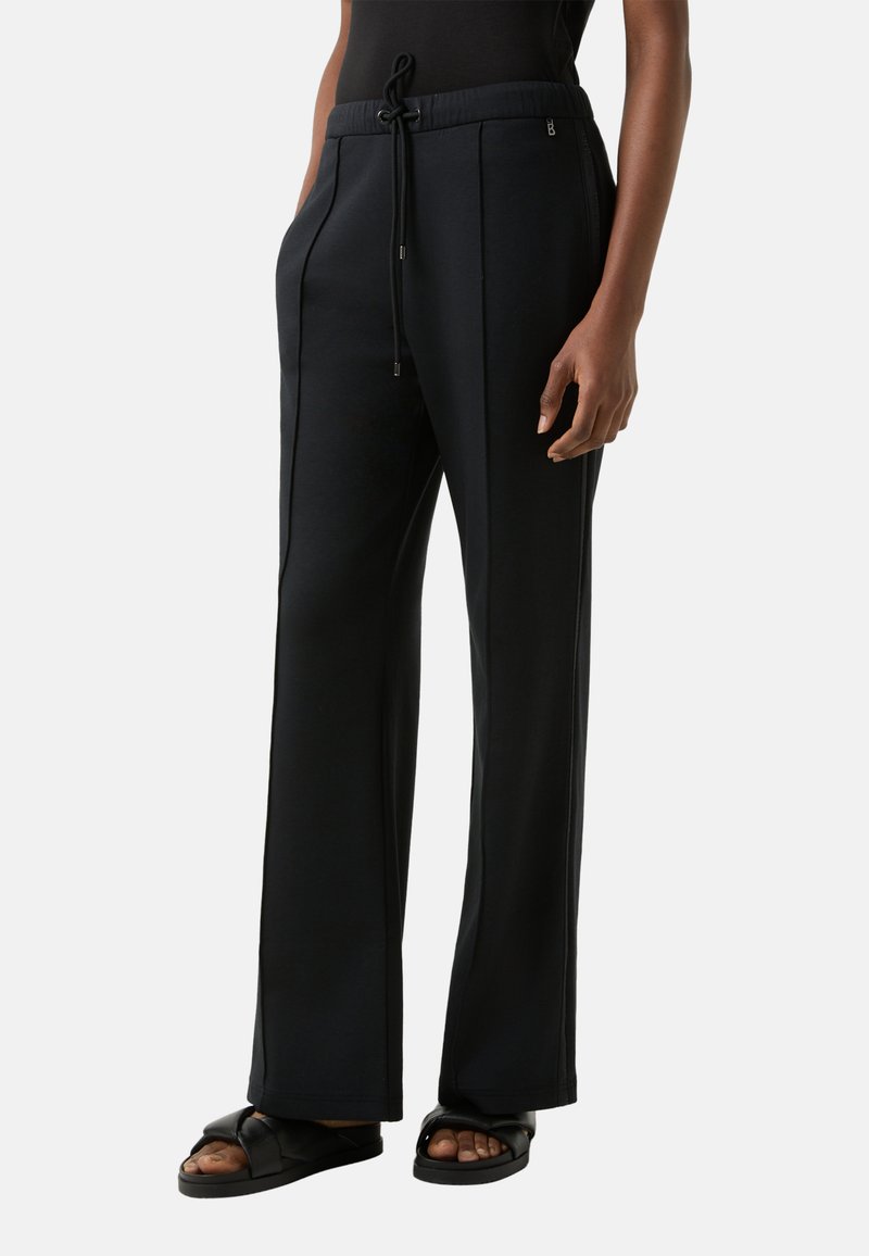 Zwarte wijde broekspijpen van zachte stof met steekzakken aan de voorkant en een elastische tailleband. Gecombineerd met zwarte sandalen met een geknoopte detail.