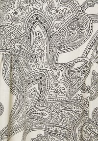 Musta-valkoinen paisley-kuvioitu kangas, jossa on monimutkaisia kukka- ja pisaramaisia muotoja teksturoidulla kermanvärisellä taustalla.