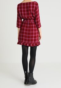 Röd och blå rutigt klänning med trekvartsärmar, midja med bälte, volangnederkant, och bärs med svarta leggings och ankelboots.