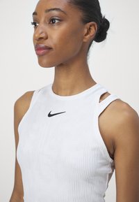 Witte sportieve tanktop met ribbeltextuur, mouwloos ontwerp en een zwart Nike-logo centraal op de borst.