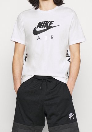 Camiseta de algodón blanca con el logo negro de "NIKE AIR" en la parte frontal, combinada con pantalones cortos de malla negros que cuentan con un dobladillo inferior gris en contraste y un logo en el lateral.
