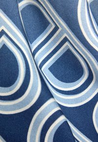 Blau gemusterter Stoff mit abwechselnd hellblauen und weißen konzentrischen Formen, glatter Textur und gefaltetem Fall.