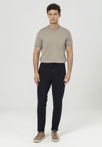 Beige korte mouw shirt in combinatie met zwarte broek met koord. Model draagt lichtbruine sneakers. Eenvoudig, casual ontwerp met een getailleerde silhouet.