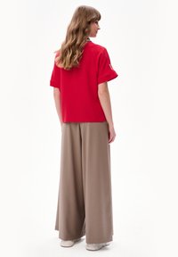 Czerwony top z krótkim rękawem i podwiniętymi mankietami, w zestawieniu z jasnobrązowymi spodniami szerokimi. Materiał wydaje się być miękki, z luźnym krojem i swobodnym stylem.