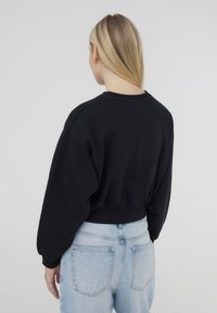 Felpa nera corta con maniche lunghe e leggermente a sbuffo. Collo rotondo e orlo a coste. Abbinata a jeans di denim azzurri a vita alta.
