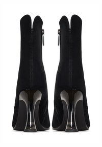 Crne gležnjače s uskim, sjajnim petama i zatvaranjem na zip. Izrađene od mekog teksturiranog materijala. Zakrivljena detalj na ovratniku na vrhu.