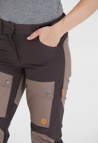 Donkerbruin en tan cargobroek van duurzaam materiaal, met meerdere zakken, zilveren hardwaren en een leren logopatch.