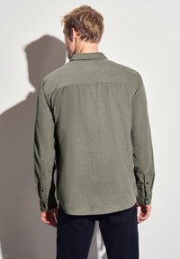 Camisa verde de manga larga con cuello, puños abotonados y un tejido texturizado. Presenta un diseño de canesú en la parte posterior y un dobladillo recto.