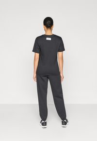 Μαύρο βαμβακερό t-shirt και ταιριαστά φούτερ παντελόνια. Απλός σχεδιασμός με ετικέτα στο πίσω μέρος. Λείο ύφασμα, άνετη εφαρμογή, κατάλληλο για καθημερινή χρήση.