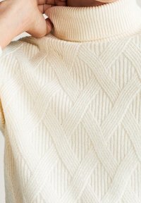 Strick-Turtleneck-Pullover in Creme mit strukturiertem Kabelmuster, ausgestattet mit einem gerippten Kragen und weichem, dickem Stoff für Wärme.