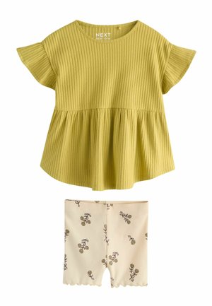 Prążkowany, musztardowo-żółty top z krótkim rękawem i rozkloszowanym dołem, połączony z kremowymi szortami ozdobionymi małymi brązowymi kwiatowymi wzorami.